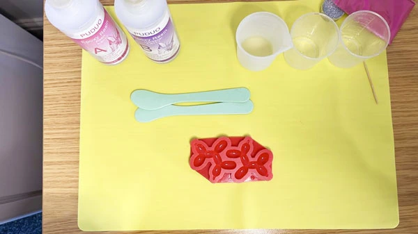 Topdown view of a silicone mat with a silicone mould, two resin bottles, beakers, and stirring sticks