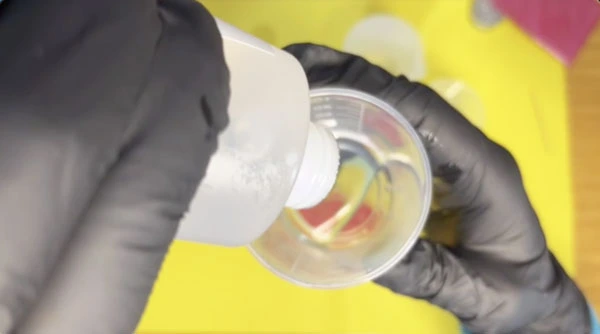 Close up of hands pouring clear resin into a mixing cup