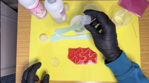 Hand adding glitter to mixing cup full of resin