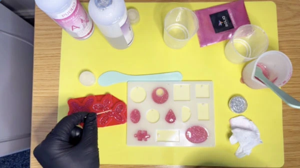 Close up of hand using a toothpick to prick bubbles on surface of resin in moulds