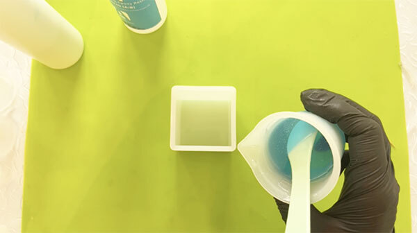 Hands mixing clear resin beside a cuboid silicone mould