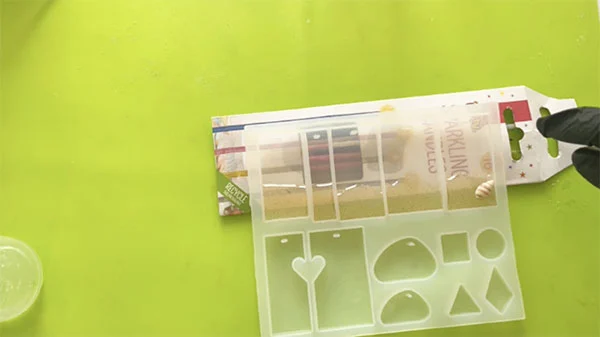 Small shell being placed in a silicone mould atop resin mixed with sand