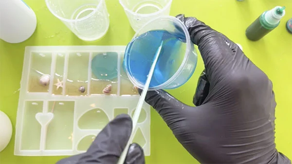 Blue resin being poured into a silicone mould that already contains a layer of sand and shells