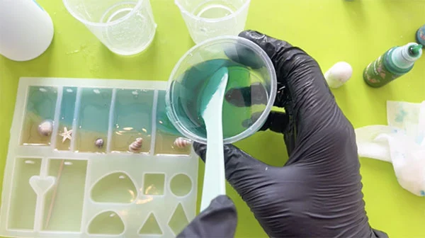 Teal coloured resin being poured into silicone moulds that already contain a layer of sandy resin and blue resin