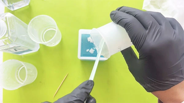 A layer of clear resin being poured into cuboid silicone mould full of blue resin and clouds
