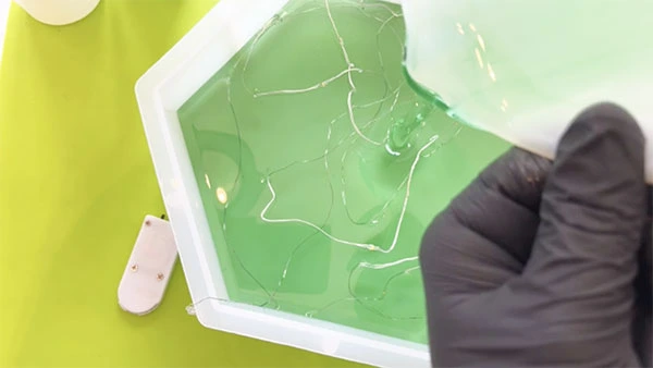 Green resin being poured into hexagonal mould with fairy lights inside it
