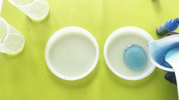A layer of blue resin being poured into a flat circular silicone mould