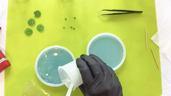 Clear resin being poured over a silicone mould containing a blue layer of resin