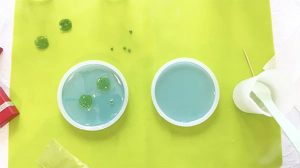 Tiny lilypads and frogs being placed in a coaster silicone mould filled with blue resin
