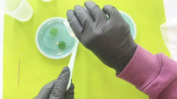 Hands pouring clear resin over a pond scene in a silicone mould