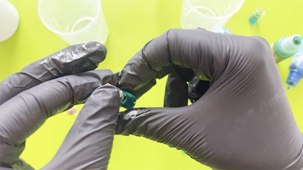 Close up of a gloved hand placing a cork lid on a tiny jar full of blue resin