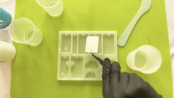 Tweezers grasping a face down sticker over a silicone mould