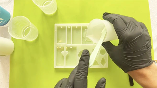 Hands pouring a thin layer of resin into a silicone mould