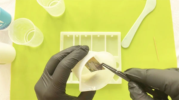 Tweezers immersing sticker in cup of resin