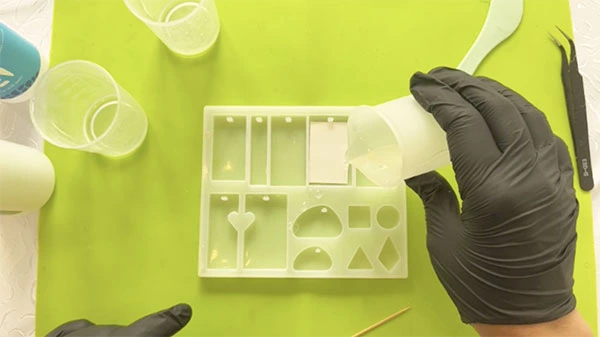Hand pouring clear resin into silicone mould with sticker in it