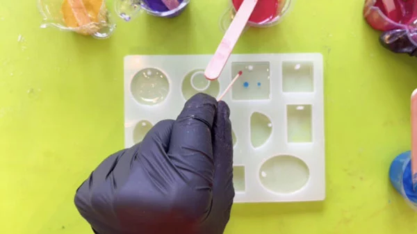 Hand using a toothpick to drop dots of coloured resin into moulds filled with clear resin