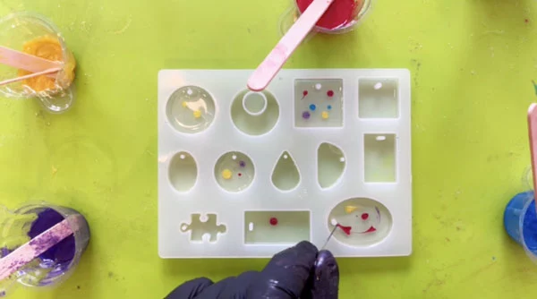 Hand dragging a needle through resin dots in silicone mould