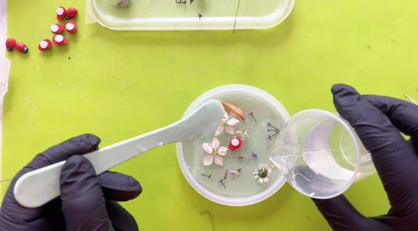 Plastic spatula drizzling clear resin over flowers in resin